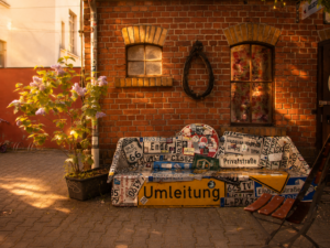 Eine Hauswand mit Ziegelsteinen. Davor steht eine Sitzbang, welche aus Auto und Straßenschilder gebaut ist.